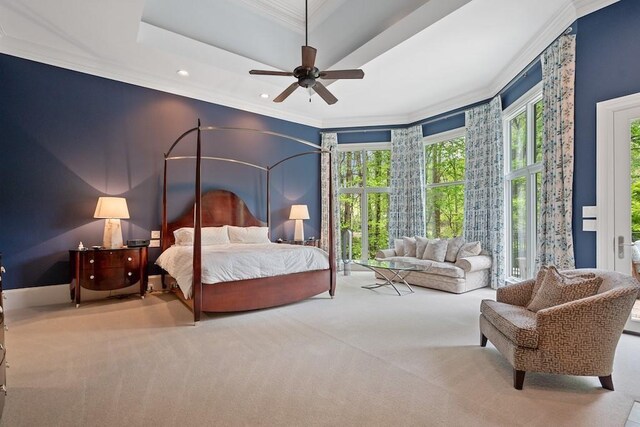 bedroom with multiple windows, light carpet, a tray ceiling, and ceiling fan