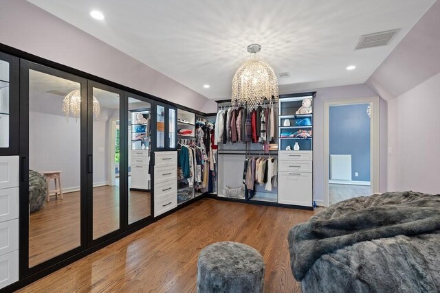 spacious closet with a chandelier, dark wood-type flooring, and vaulted ceiling