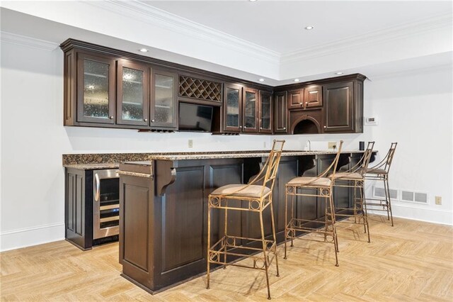 bar with dark brown cabinets, crown molding, wine cooler, and light parquet flooring