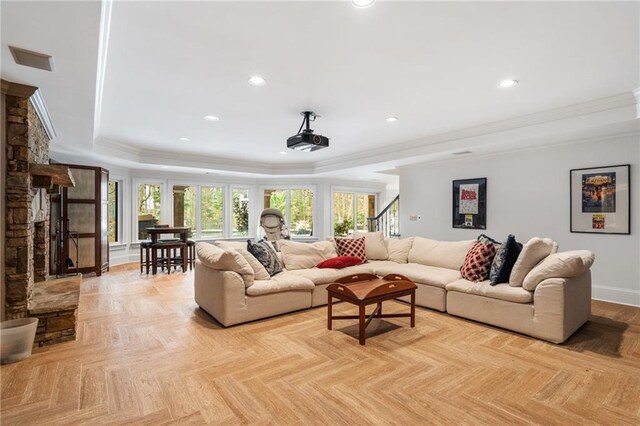 living room featuring a stone fireplace, a raised ceiling, ornamental molding, and light parquet floors