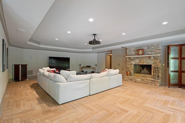 living room with light parquet flooring, a raised ceiling, ornamental molding, and a stone fireplace