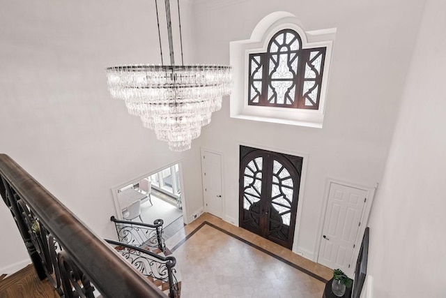 entrance foyer with tile patterned floors, french doors, a towering ceiling, and an inviting chandelier