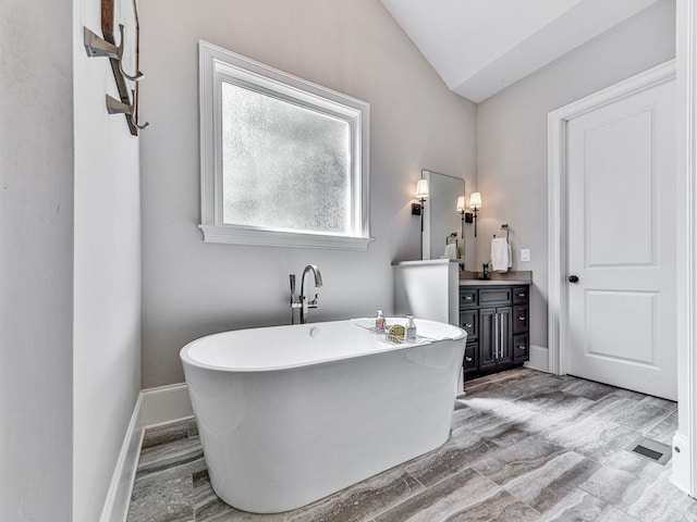5039 Towne Lake Hls N, Woodstock, GA 30189 - bathroom with vaulted ceiling, vanity, a freestanding tub, and baseboards