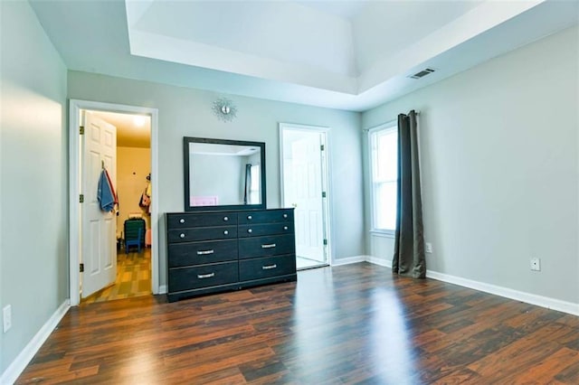 bedroom featuring dark wood-type flooring, visible vents, baseboards, and a raised ceiling