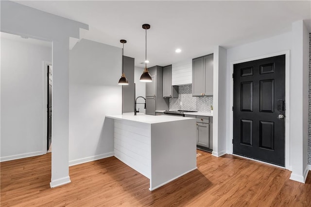 kitchen featuring light hardwood / wood-style floors, tasteful backsplash, kitchen peninsula, pendant lighting, and gray cabinetry