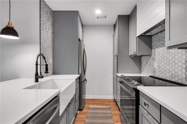 kitchen featuring sink, decorative light fixtures, light hardwood / wood-style flooring, gray cabinets, and appliances with stainless steel finishes