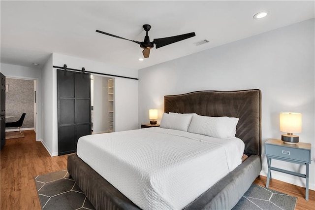 bedroom with ceiling fan, a walk in closet, a barn door, and wood-type flooring