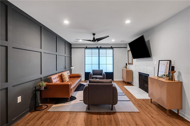 living room with a tiled fireplace, ceiling fan, and light hardwood / wood-style flooring