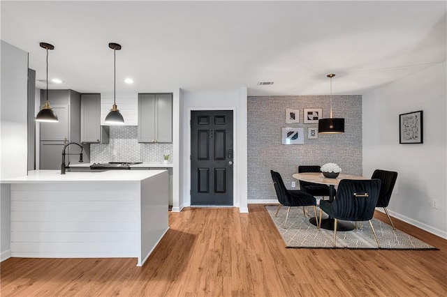 kitchen featuring gray cabinets, light wood-type flooring, brick wall, sink, and backsplash