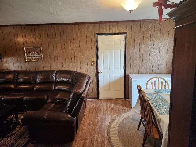 living room featuring wood-type flooring, wooden walls, a textured ceiling, and ornamental molding