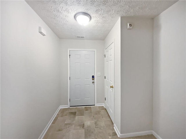 doorway to outside with a textured ceiling, visible vents, and baseboards