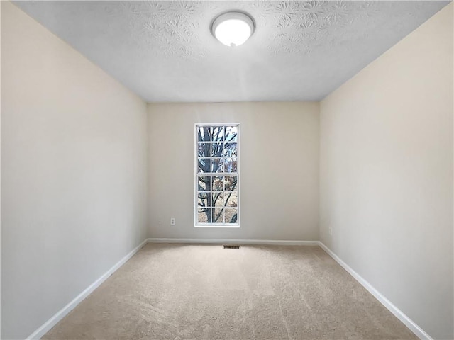 carpeted spare room with baseboards, visible vents, and a textured ceiling