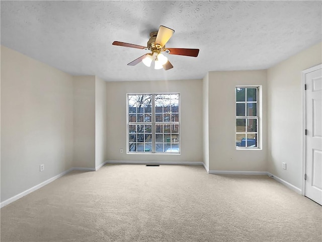 carpeted spare room featuring a textured ceiling, ceiling fan, and baseboards