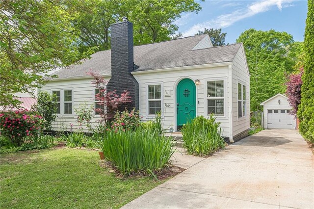 view of front of home featuring a detached garage, concrete driveway, a chimney, an outbuilding, and a front yard
