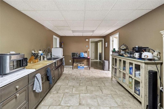 kitchen with dark brown cabinetry, stainless steel microwave, light countertops, a paneled ceiling, and a sink