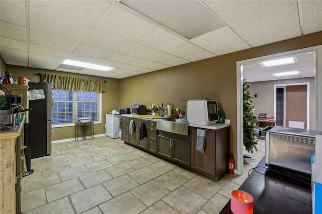 kitchen featuring light countertops, freestanding refrigerator, a sink, dark brown cabinets, and a drop ceiling