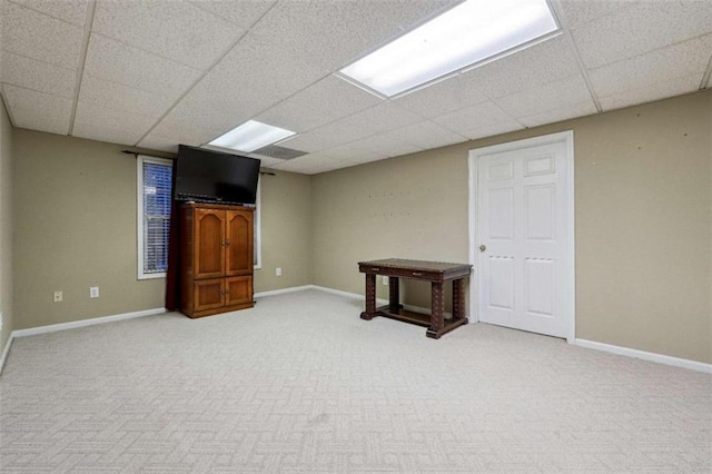 finished basement featuring a drop ceiling, light carpet, and baseboards