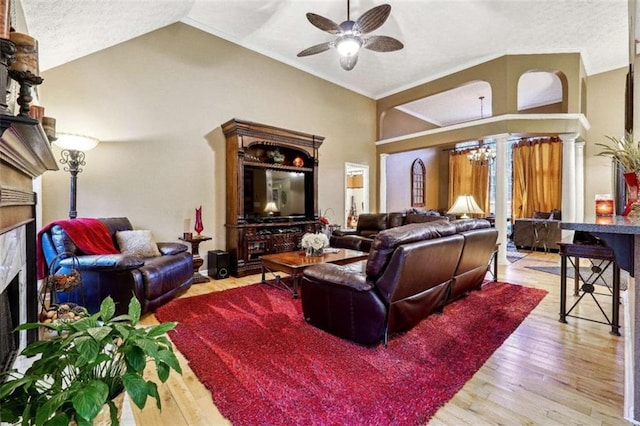 living room with vaulted ceiling, a fireplace, light wood finished floors, and ceiling fan with notable chandelier