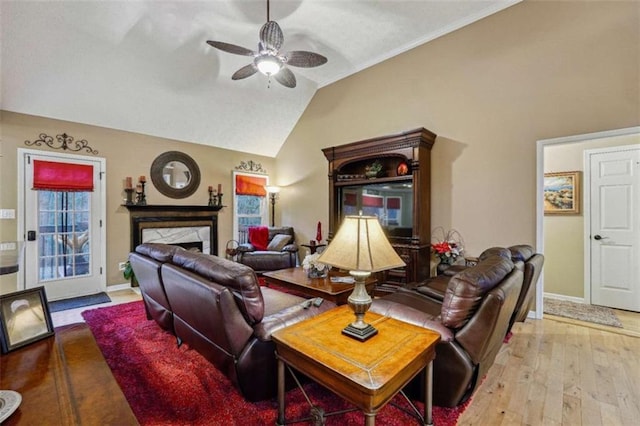 living area featuring ceiling fan, a fireplace, baseboards, vaulted ceiling, and light wood finished floors