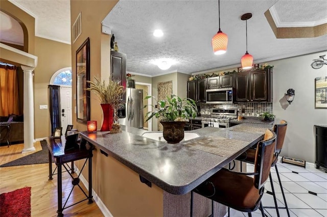 kitchen with a breakfast bar, decorative columns, appliances with stainless steel finishes, dark brown cabinets, and a peninsula