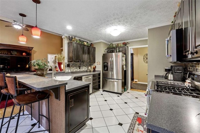 kitchen featuring stainless steel appliances, a peninsula, a sink, dark countertops, and a kitchen bar