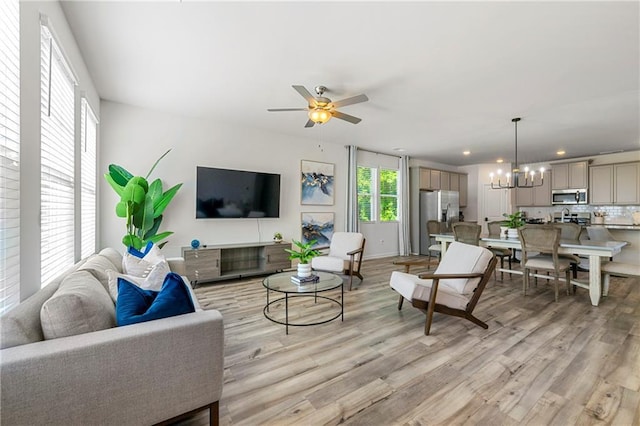 living area with ceiling fan with notable chandelier, light wood finished floors, and recessed lighting