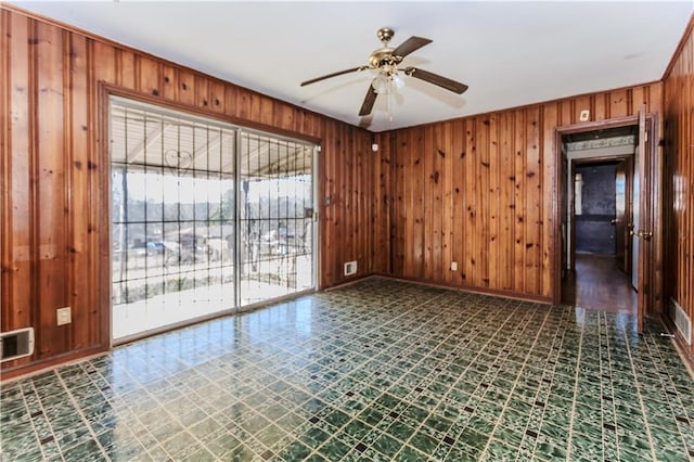 unfurnished room with visible vents, baseboards, ceiling fan, tile patterned floors, and wood walls