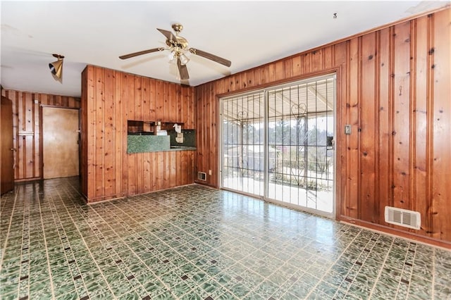 spare room featuring ceiling fan, visible vents, wood walls, and tile patterned floors