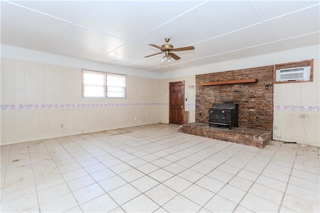 unfurnished living room featuring a wall mounted air conditioner, tile patterned floors, a wood stove, and a ceiling fan