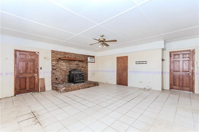 unfurnished living room featuring a wood stove, ceiling fan, and light tile patterned flooring