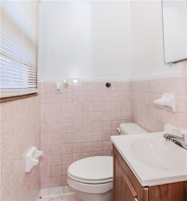 half bath featuring toilet, a wainscoted wall, tile walls, and vanity