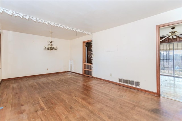 spare room with baseboards, visible vents, hardwood / wood-style floors, and ceiling fan with notable chandelier