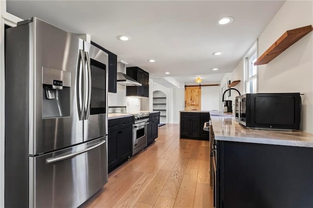 kitchen featuring sink, stainless steel appliances, a barn door, wall chimney exhaust hood, and light wood-type flooring