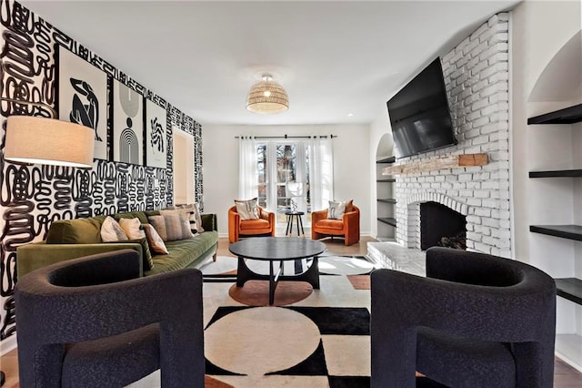 living room with a brick fireplace, built in shelves, and hardwood / wood-style floors