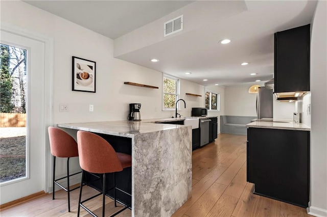 kitchen featuring a breakfast bar, stainless steel refrigerator, light hardwood / wood-style floors, kitchen peninsula, and light stone countertops