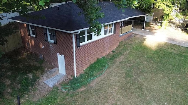 exterior space featuring a yard, brick siding, roof with shingles, and fence