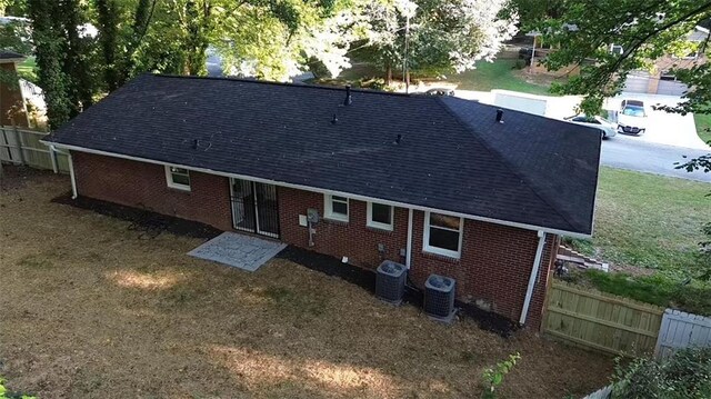 rear view of property with central air condition unit, fence, brick siding, and roof with shingles