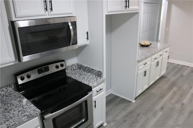 kitchen featuring light wood-type flooring, appliances with stainless steel finishes, light stone countertops, and white cabinetry