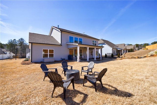 back of property with a shingled roof, an outdoor fire pit, and a patio