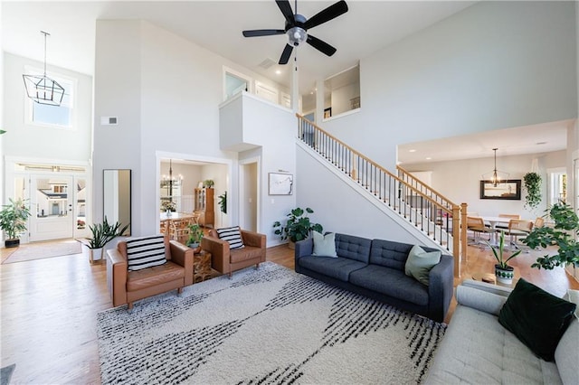 living room featuring stairs, ceiling fan with notable chandelier, wood finished floors, and visible vents