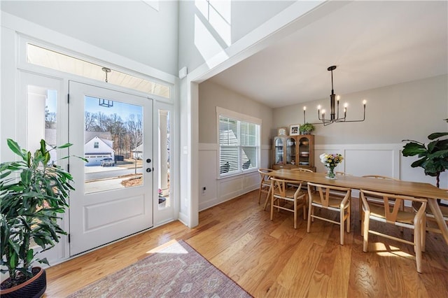 entryway featuring a notable chandelier, a decorative wall, a towering ceiling, light wood-style floors, and wainscoting