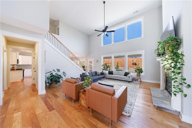 living area with visible vents, baseboards, a ceiling fan, stairway, and light wood finished floors