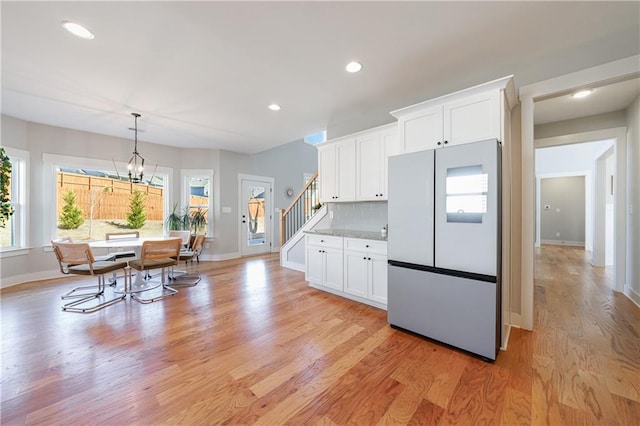 kitchen with decorative backsplash, freestanding refrigerator, light wood-style floors, white cabinetry, and a notable chandelier