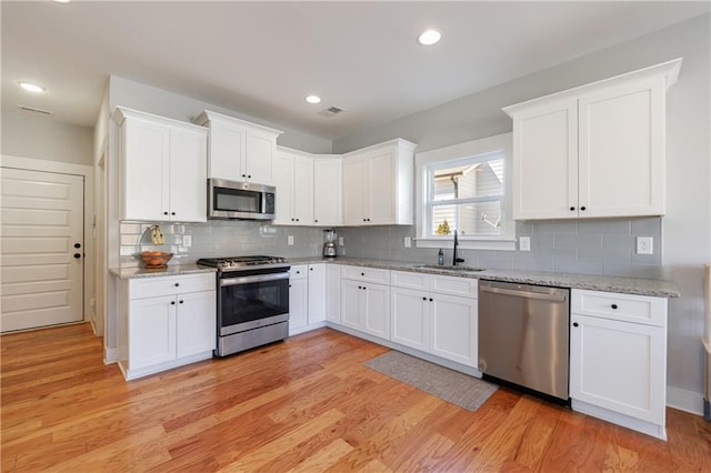 kitchen featuring appliances with stainless steel finishes, light wood-type flooring, white cabinets, and light stone counters