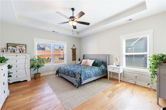 bedroom with a raised ceiling, baseboards, visible vents, and light wood finished floors