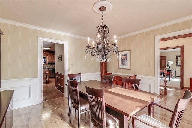 dining area with crown molding, light hardwood / wood-style floors, and an inviting chandelier