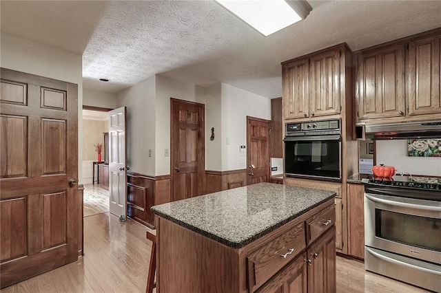 kitchen with a textured ceiling, a kitchen island, light hardwood / wood-style flooring, dark stone countertops, and black oven