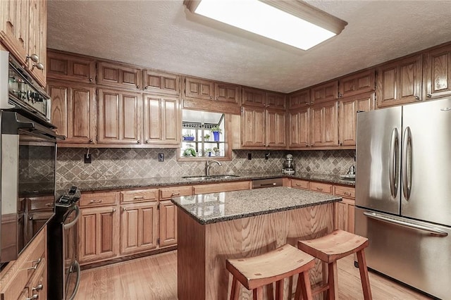 kitchen with appliances with stainless steel finishes, a breakfast bar, sink, light hardwood / wood-style floors, and a kitchen island