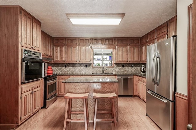 kitchen with a kitchen breakfast bar, stainless steel appliances, sink, a center island, and light hardwood / wood-style floors