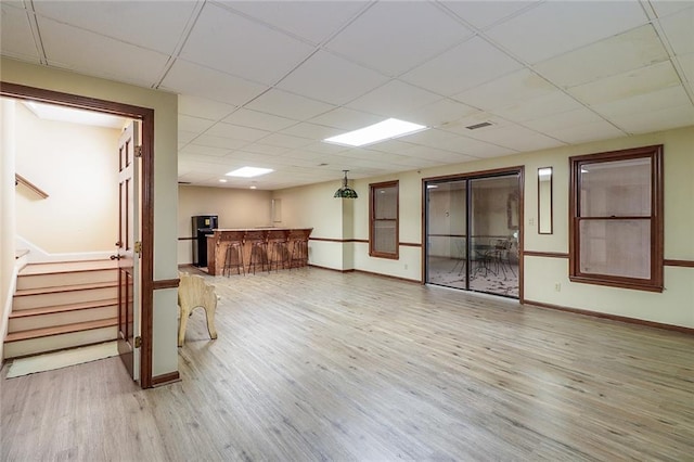 basement featuring a drop ceiling, wood-type flooring, and bar area